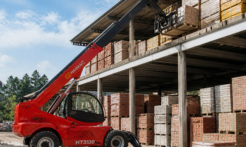 HAMAC HT3510 telehandler stacking pallets of bricks, tiles, insulation and precast elements on mezzanine storage levels inside a logistics and precast yard in Southeast Asia or Latin America